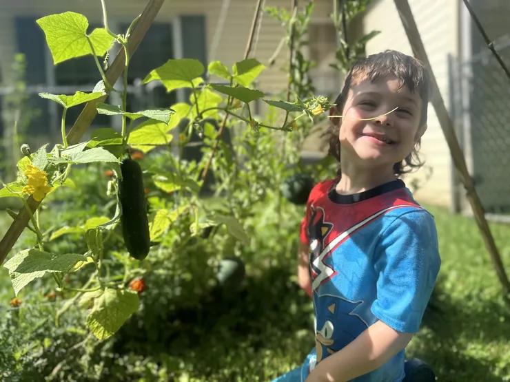 Boy smiling among cucumber vines in the CBCA garden