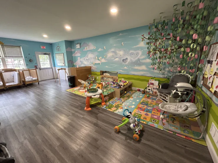 Infant room with a hand-painted sky mural at CB Children's Academy