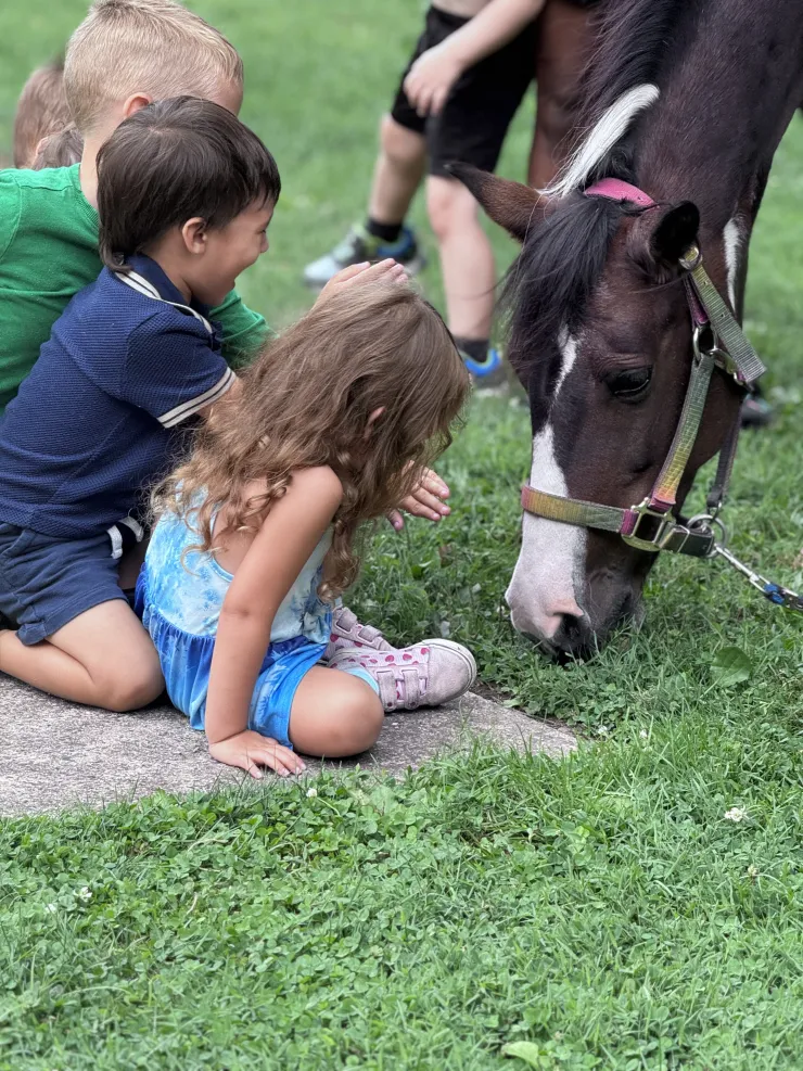 Children gently petting a pony grazing on the grass at CBCA