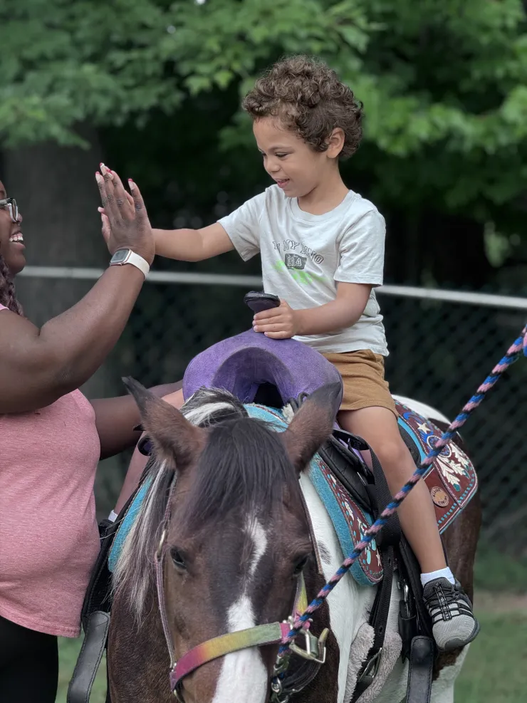 Child high-fiving a teacher while riding a pony at CBCA
