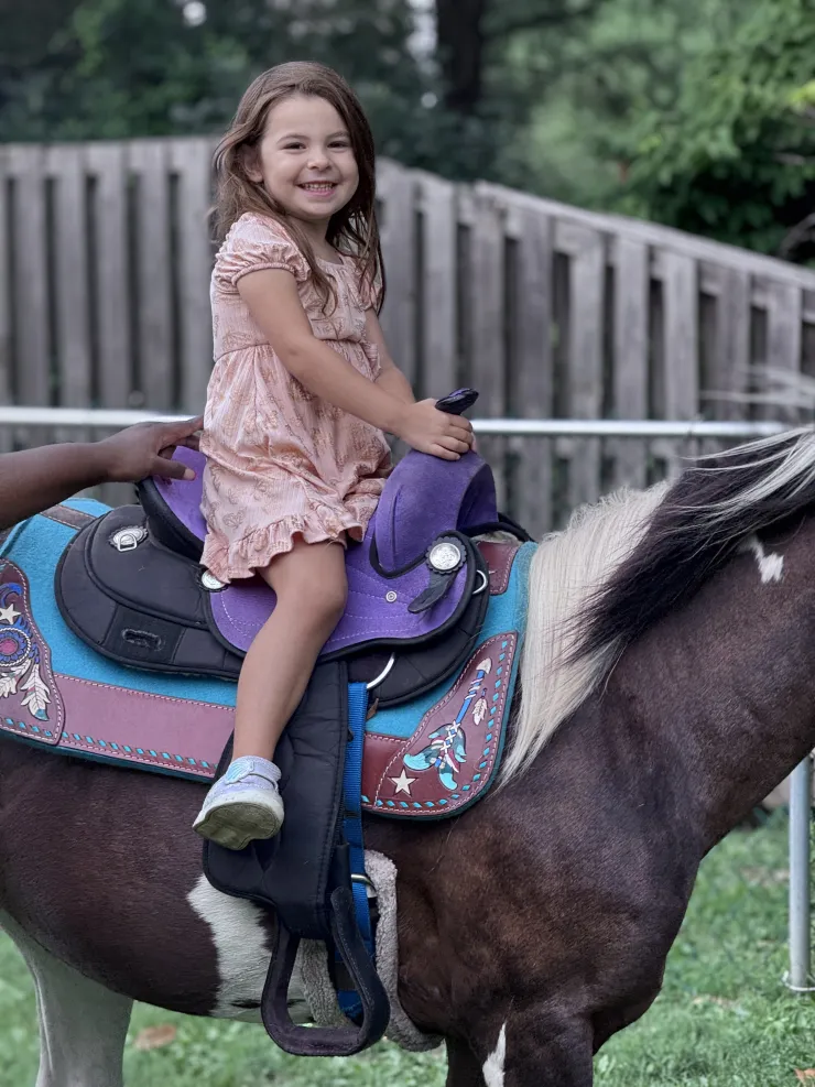 Girl in a dress smiling on a pony at CBCA